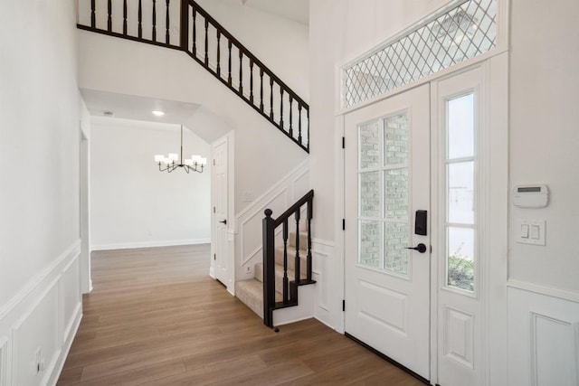 entrance foyer with wood finished floors, a decorative wall, a chandelier, a towering ceiling, and stairs