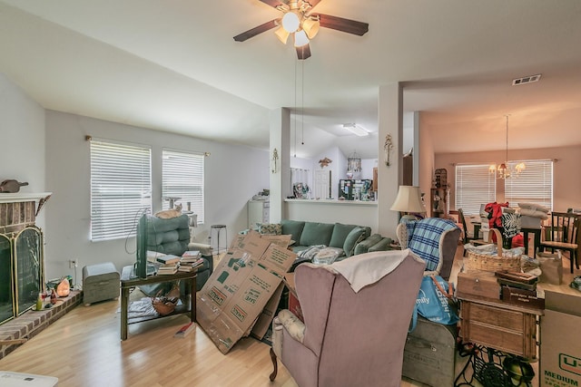 living area featuring visible vents, a brick fireplace, lofted ceiling, light wood-style flooring, and ceiling fan with notable chandelier