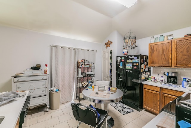 kitchen featuring light countertops, vaulted ceiling, black fridge with ice dispenser, tasteful backsplash, and brown cabinets