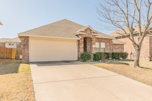 view of front of property featuring cooling unit, fence, roof with shingles, an attached garage, and brick siding