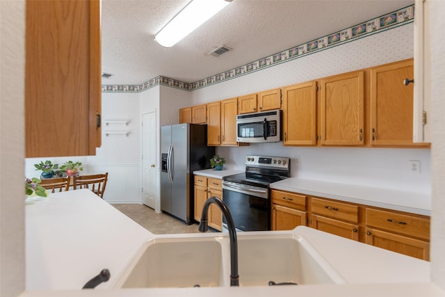 kitchen featuring visible vents, a sink, a textured ceiling, appliances with stainless steel finishes, and wallpapered walls