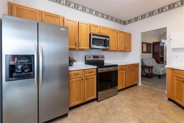 kitchen with wallpapered walls, stainless steel appliances, light countertops, a textured ceiling, and brown cabinets