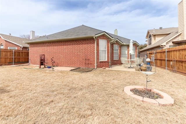 back of property featuring a patio, a yard, a fenced backyard, a chimney, and brick siding