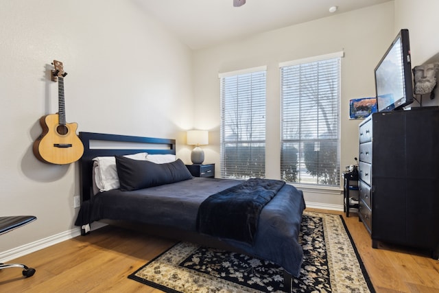 bedroom featuring light wood finished floors, multiple windows, lofted ceiling, and baseboards