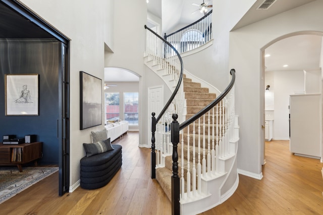 staircase featuring hardwood / wood-style floors, visible vents, arched walkways, and a ceiling fan