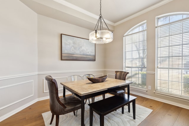 dining area featuring a wainscoted wall, ornamental molding, a decorative wall, and wood finished floors