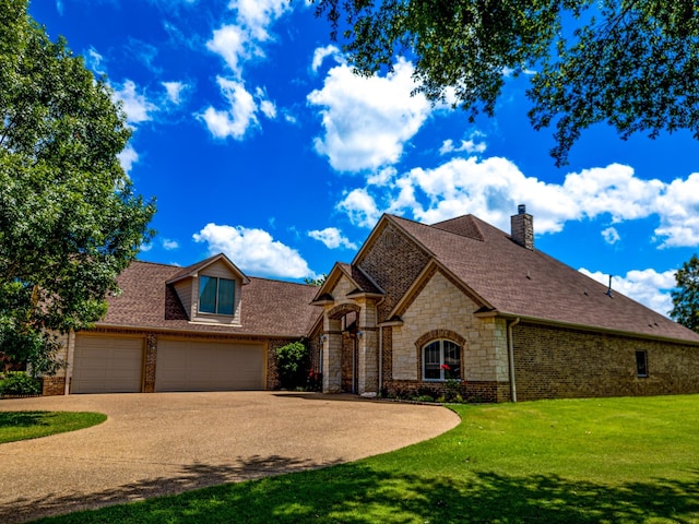 french country inspired facade featuring a garage, driveway, a front yard, and roof with shingles