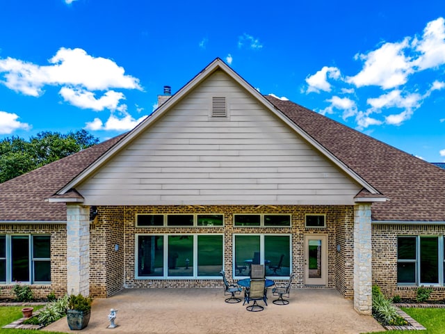 rear view of property featuring a patio, brick siding, and roof with shingles