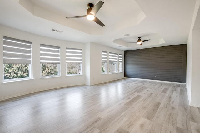 unfurnished room with visible vents, light wood-style flooring, a ceiling fan, baseboards, and a raised ceiling