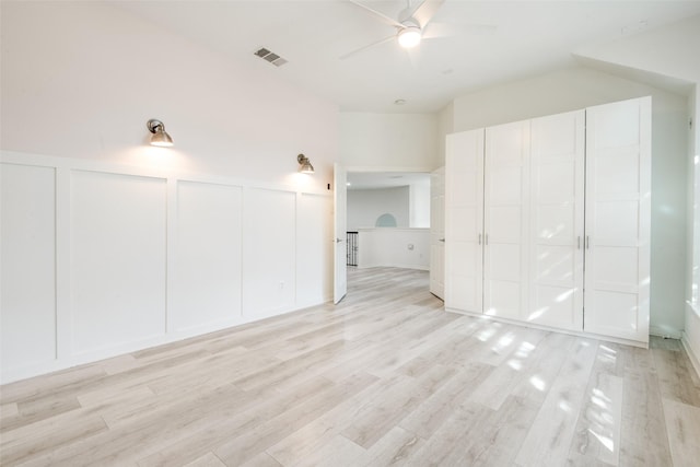 unfurnished bedroom featuring a decorative wall, visible vents, light wood finished floors, and wainscoting