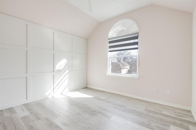 empty room featuring a decorative wall, light wood-type flooring, ceiling fan, and vaulted ceiling