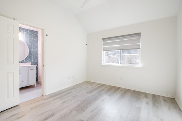 unfurnished bedroom with connected bathroom, baseboards, light wood-style floors, and vaulted ceiling