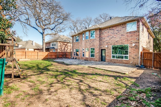 rear view of house featuring a lawn, a fenced backyard, a playground, brick siding, and a patio area