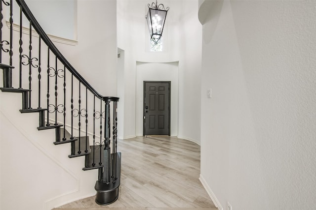 foyer with stairway, baseboards, a high ceiling, and wood finished floors