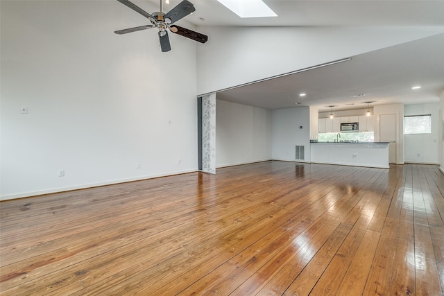 unfurnished living room featuring baseboards, visible vents, a skylight, ceiling fan, and wood-type flooring