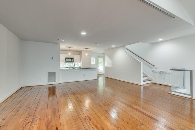 unfurnished living room with stairs, visible vents, and light wood finished floors