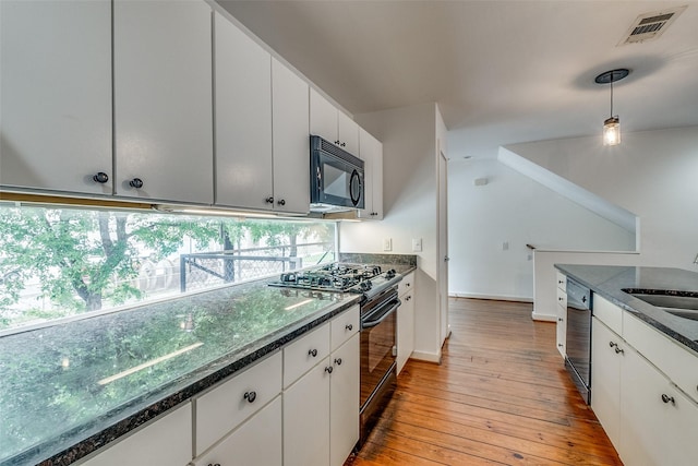 kitchen featuring visible vents, light wood-type flooring, dark stone countertops, hanging light fixtures, and black appliances