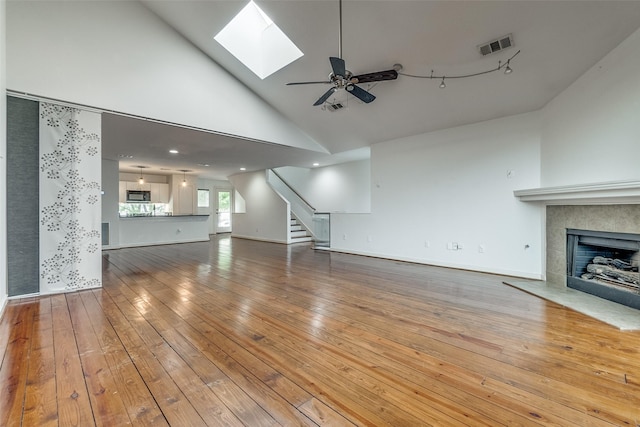 unfurnished living room with visible vents, a tiled fireplace, stairs, hardwood / wood-style floors, and a skylight