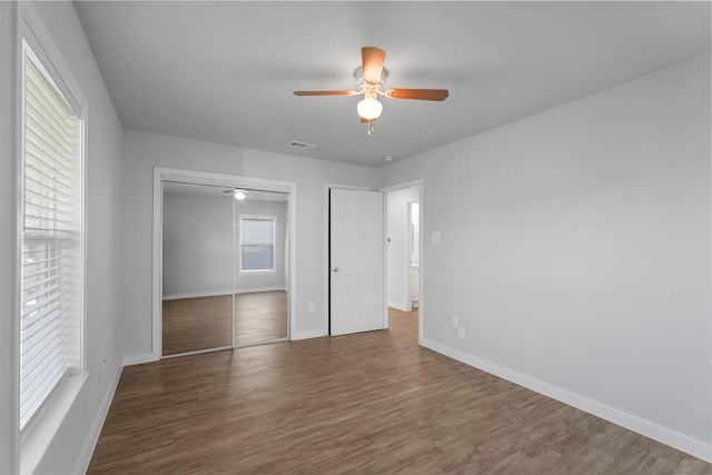 unfurnished bedroom with wood finished floors, visible vents, baseboards, ceiling fan, and a closet