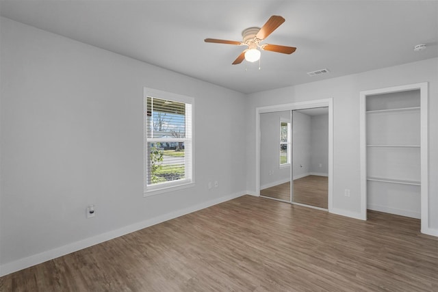 unfurnished bedroom with visible vents, two closets, baseboards, and wood finished floors