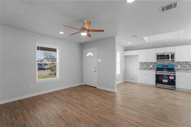 unfurnished living room with visible vents, baseboards, a skylight, and light wood-style flooring