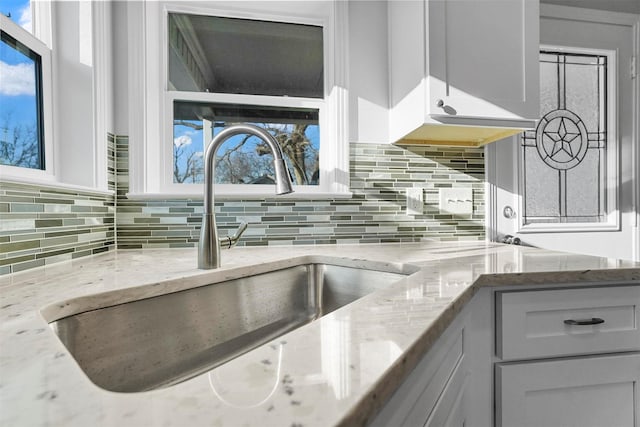 kitchen with light stone counters, backsplash, and a sink