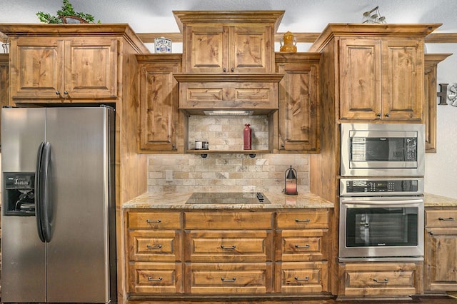 kitchen with tasteful backsplash, appliances with stainless steel finishes, brown cabinetry, and light stone countertops