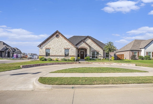 french provincial home featuring stone siding, driveway, and a front lawn