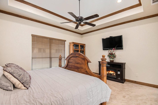 bedroom with baseboards, a tray ceiling, a glass covered fireplace, crown molding, and light colored carpet