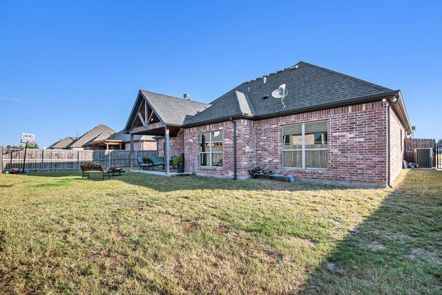 back of property featuring brick siding, a lawn, fence, and a shingled roof