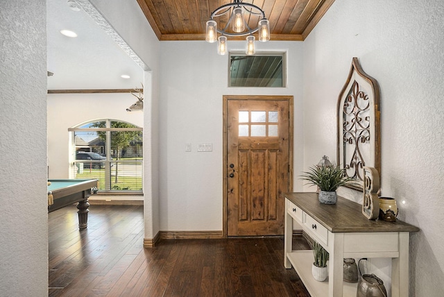 entrance foyer with dark wood-type flooring, wooden ceiling, crown molding, baseboards, and a chandelier