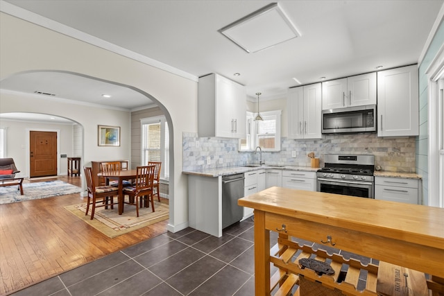 kitchen featuring dark tile patterned flooring, a sink, appliances with stainless steel finishes, crown molding, and decorative backsplash