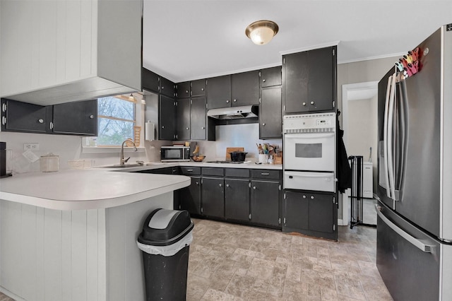 kitchen featuring a warming drawer, a sink, under cabinet range hood, stainless steel appliances, and light countertops