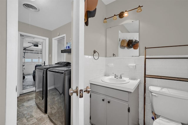 bathroom featuring visible vents, washing machine and dryer, toilet, vanity, and tile walls