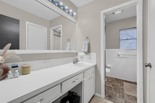 bathroom featuring toilet, tile walls, wainscoting, and vanity