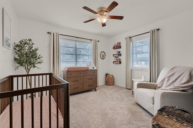 bedroom with light carpet, multiple windows, a crib, and a ceiling fan