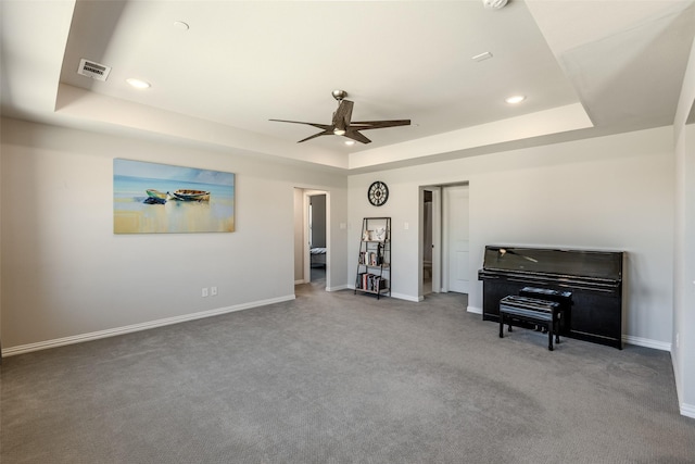 living area with visible vents, ceiling fan, baseboards, and a tray ceiling