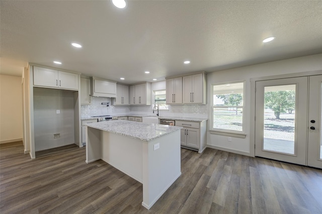 kitchen featuring a kitchen island, dark wood-type flooring, light stone counters, decorative backsplash, and stainless steel dishwasher