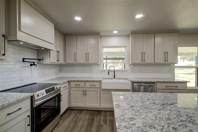 kitchen featuring a sink, light stone counters, recessed lighting, appliances with stainless steel finishes, and dark wood-style flooring