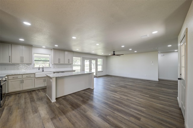 kitchen with visible vents, a kitchen island, a sink, dark wood-type flooring, and tasteful backsplash