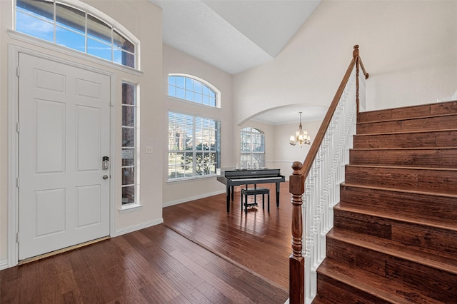 foyer entrance with dark wood-style flooring, arched walkways, baseboards, a chandelier, and stairs