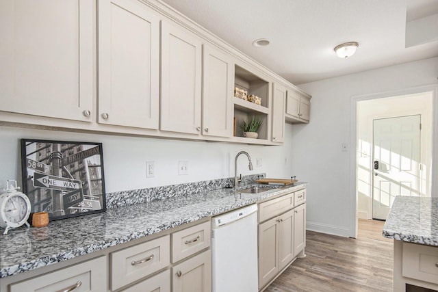 kitchen with a sink, open shelves, light wood finished floors, light stone countertops, and dishwasher