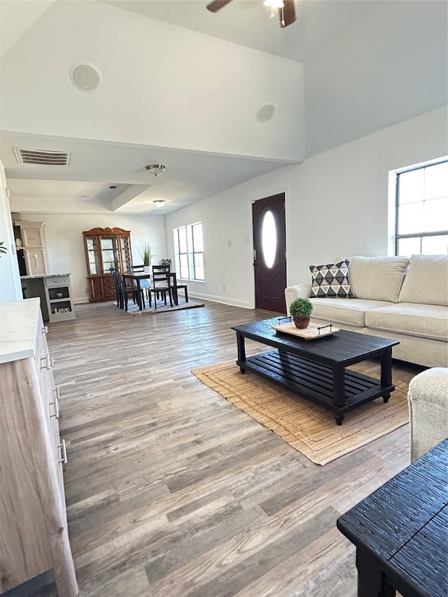 living room with visible vents, high vaulted ceiling, a ceiling fan, wood finished floors, and baseboards