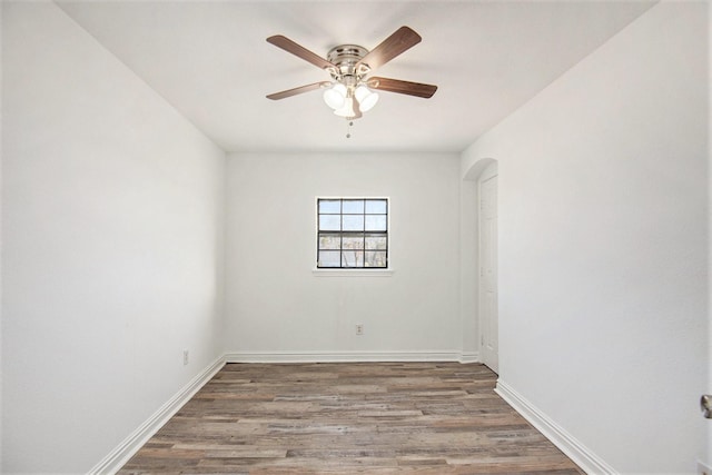 empty room with baseboards, wood finished floors, arched walkways, and ceiling fan