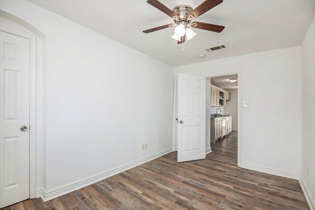 unfurnished bedroom with visible vents, baseboards, dark wood-style floors, a ceiling fan, and a sink