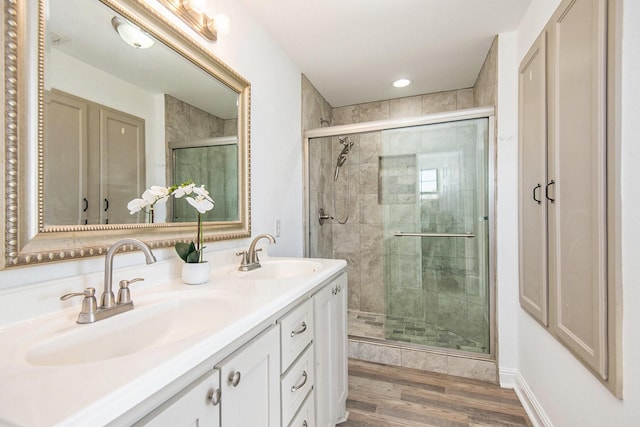 full bathroom with double vanity, a shower stall, wood finished floors, and a sink