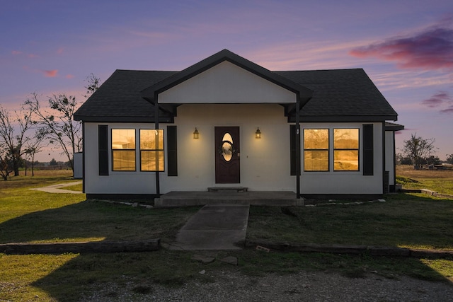 view of front of home featuring a front yard, roof with shingles, and stucco siding