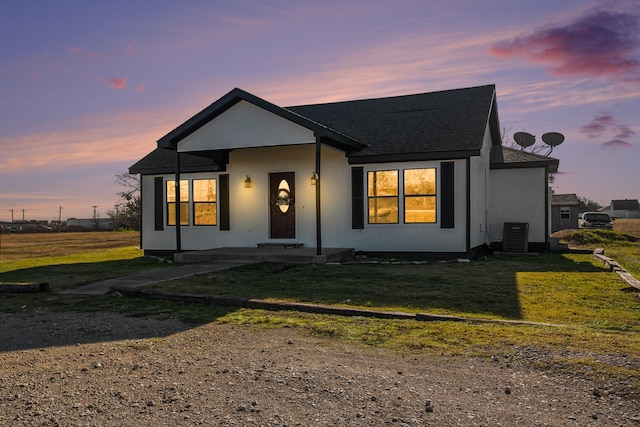 view of front of property with central air condition unit, a lawn, and roof with shingles