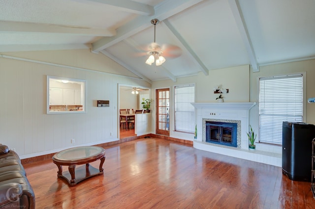 living area featuring lofted ceiling with beams, wood finished floors, ceiling fan, and a tile fireplace