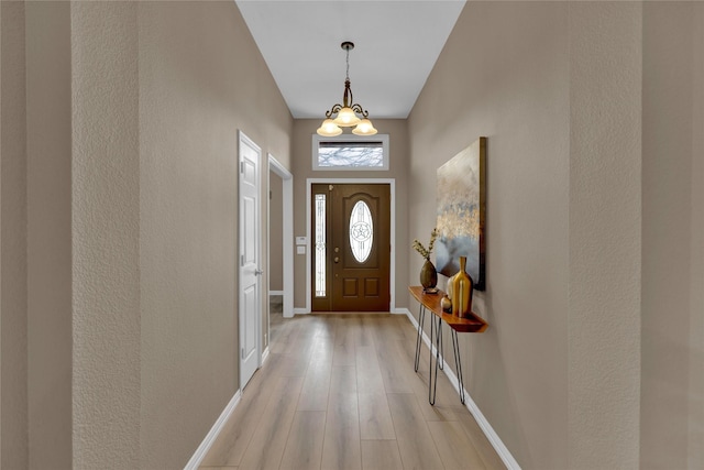 foyer entrance featuring an inviting chandelier, baseboards, and light wood-style floors